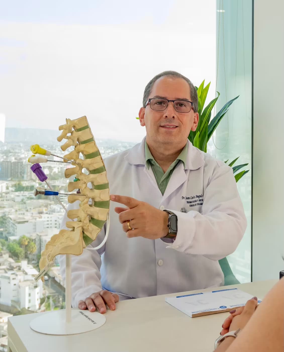 Dr. Juan Carlos Angulo Totesaut explica a una paciente un modelo de columna lumbar en su consultorio